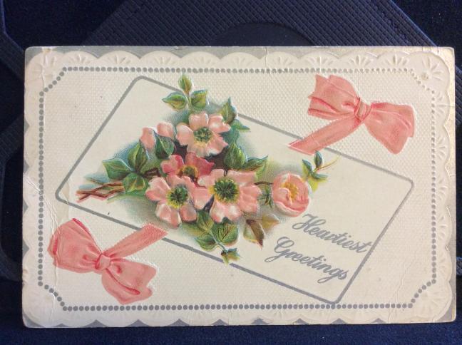 back of card. picture of flowers and a pink ribbon with the writing Heartiest Greetings.